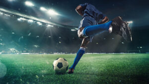 夜、サッカースタジアムのピッチでサッカーボールを蹴ろうとする男性